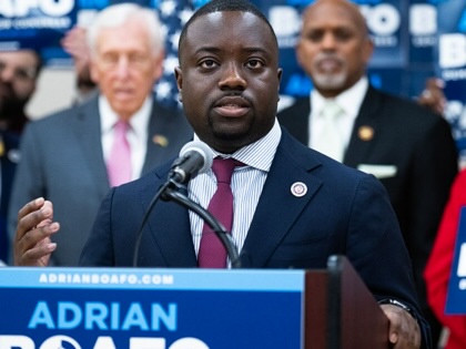Adrian Boafo speaking at a podium with his name on it while supporters look on.