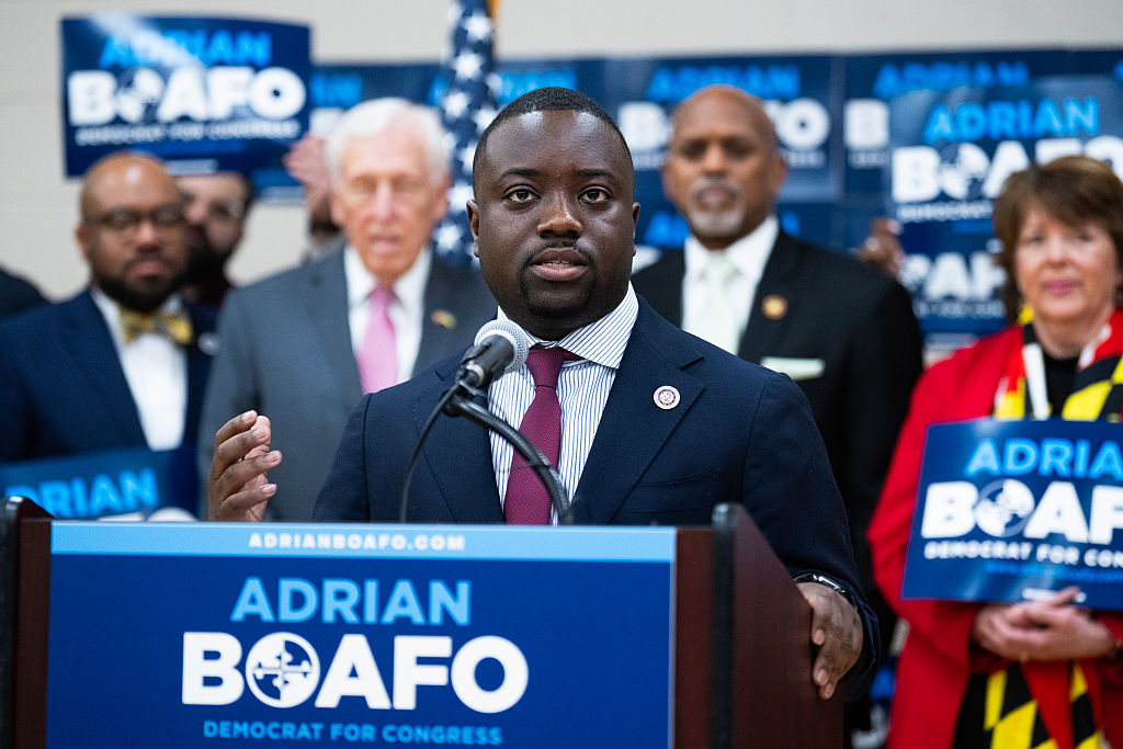 Adrian Boafo speaking at a podium with his name on it while supporters look on.