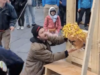 A man holds a head in a guillotine while a crowd looks on.