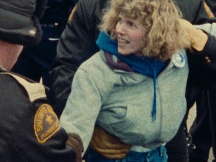 A screenshot from <cite>American Dream</cite> by Barbara Kopple, depicting an angry woman being restrained by police.