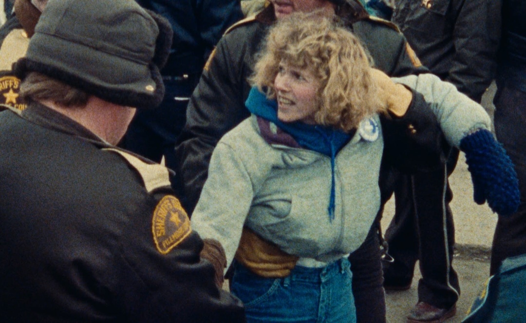 A screenshot from <cite>American Dream</cite> by Barbara Kopple, depicting an angry woman being restrained by police.