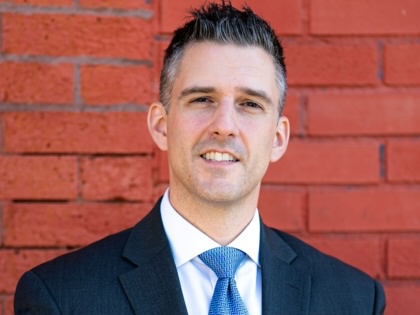 Portrait of Adam Bojak in a suit against a brick wall.