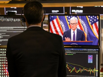 A man stands facing four TVs at the New York Stock Exchange, one showing Fed chair Jeremy Powell. 