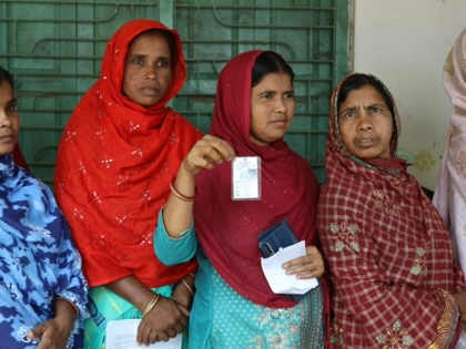 Five women standing in a line, one holding up a white piece of paper.