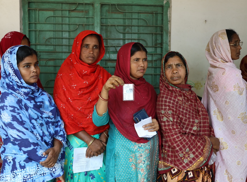 Five women standing in a line, one holding up a white piece of paper.