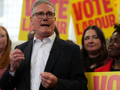 Keir Starmer gesturing while speaking to a crowd holding signs that say "Vote Labour."