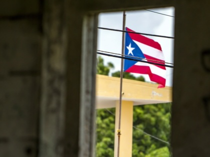A Puerto Rican flag flies through a doorway in a cement wall. 