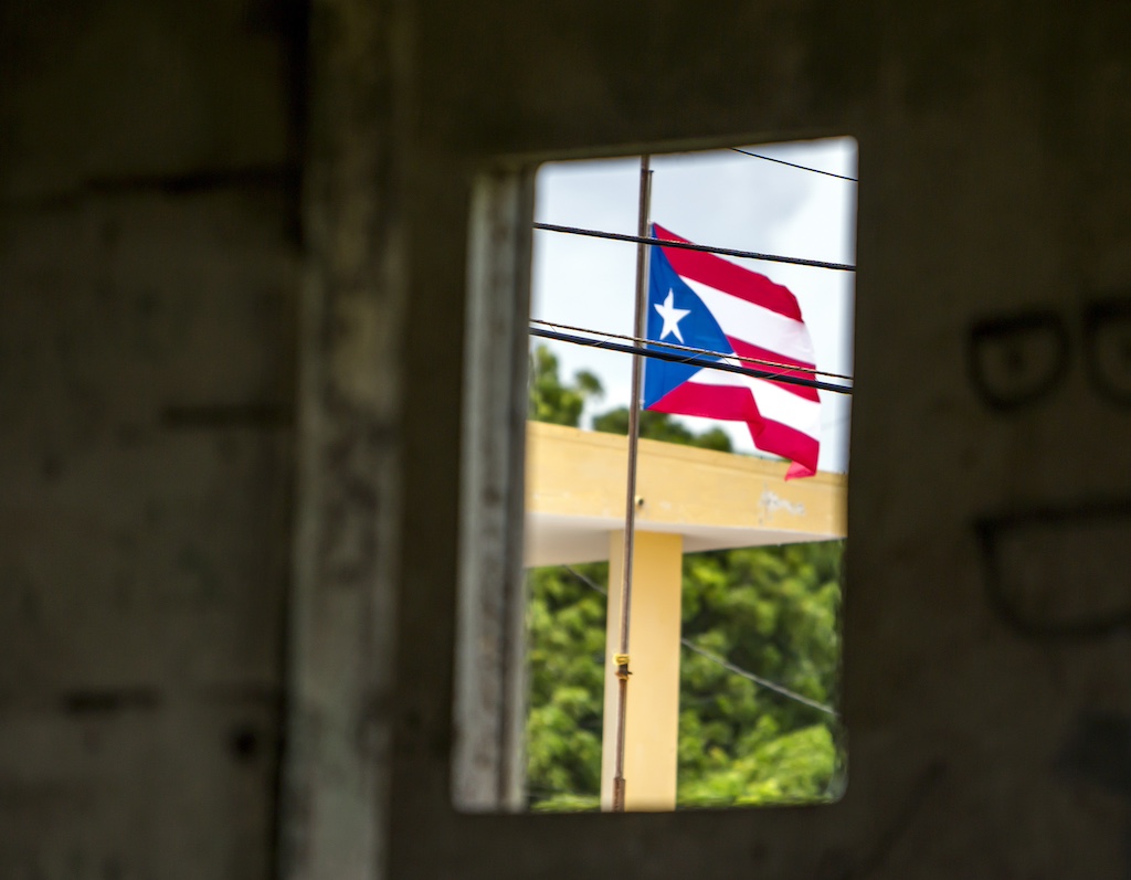 A Puerto Rican flag flies through a doorway in a cement wall. 