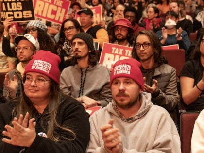 A crowd of people, some holding up placards that say "Tax the Rich" and some wearing hats that say "Democratic Socialists of America."