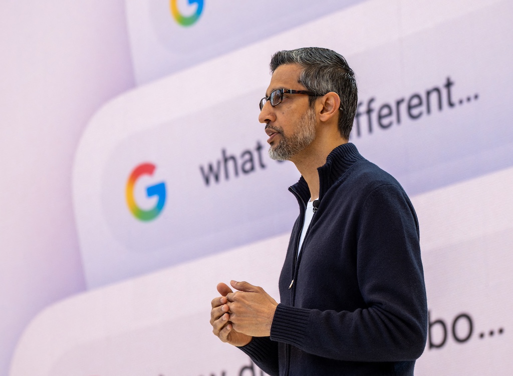 Google CEO Sundar Pichai speaking with the Google icon and search bar in the background.