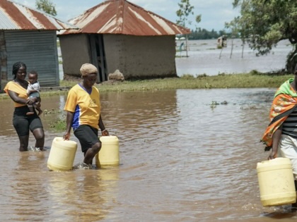 Three women trudge through a flooded street carrying water containers and one child.
