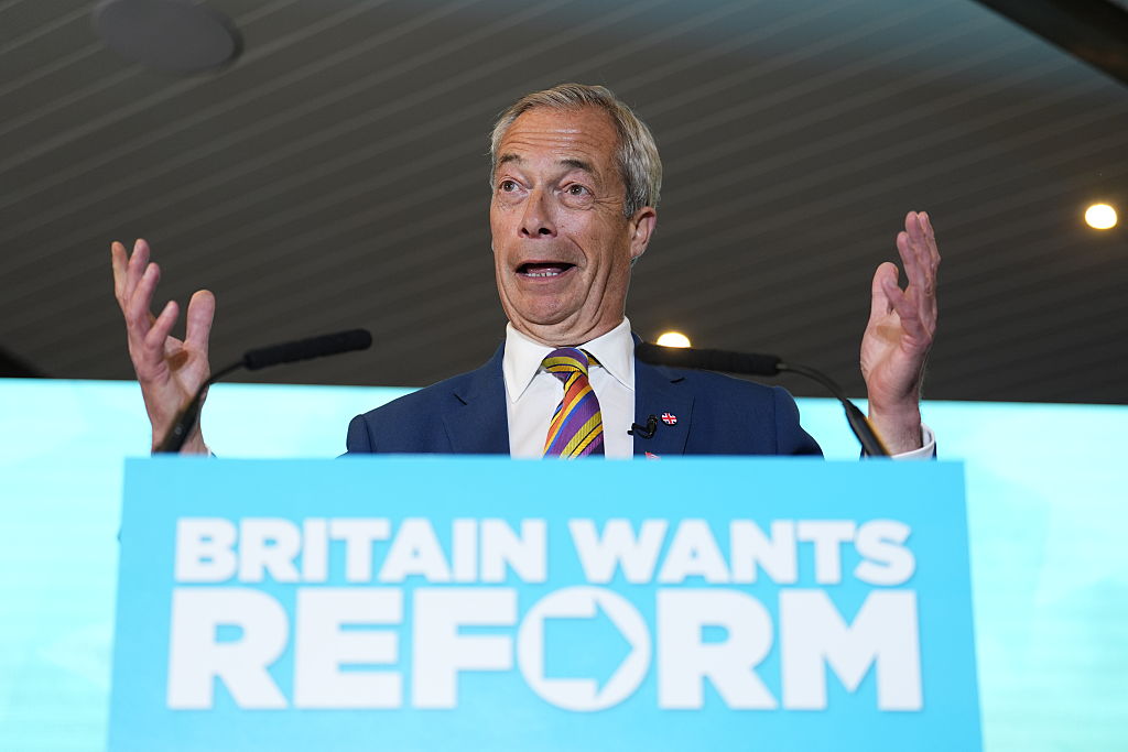 Nigel Farage gestures while speaking at a podium that reads "Britain Wants Reform."