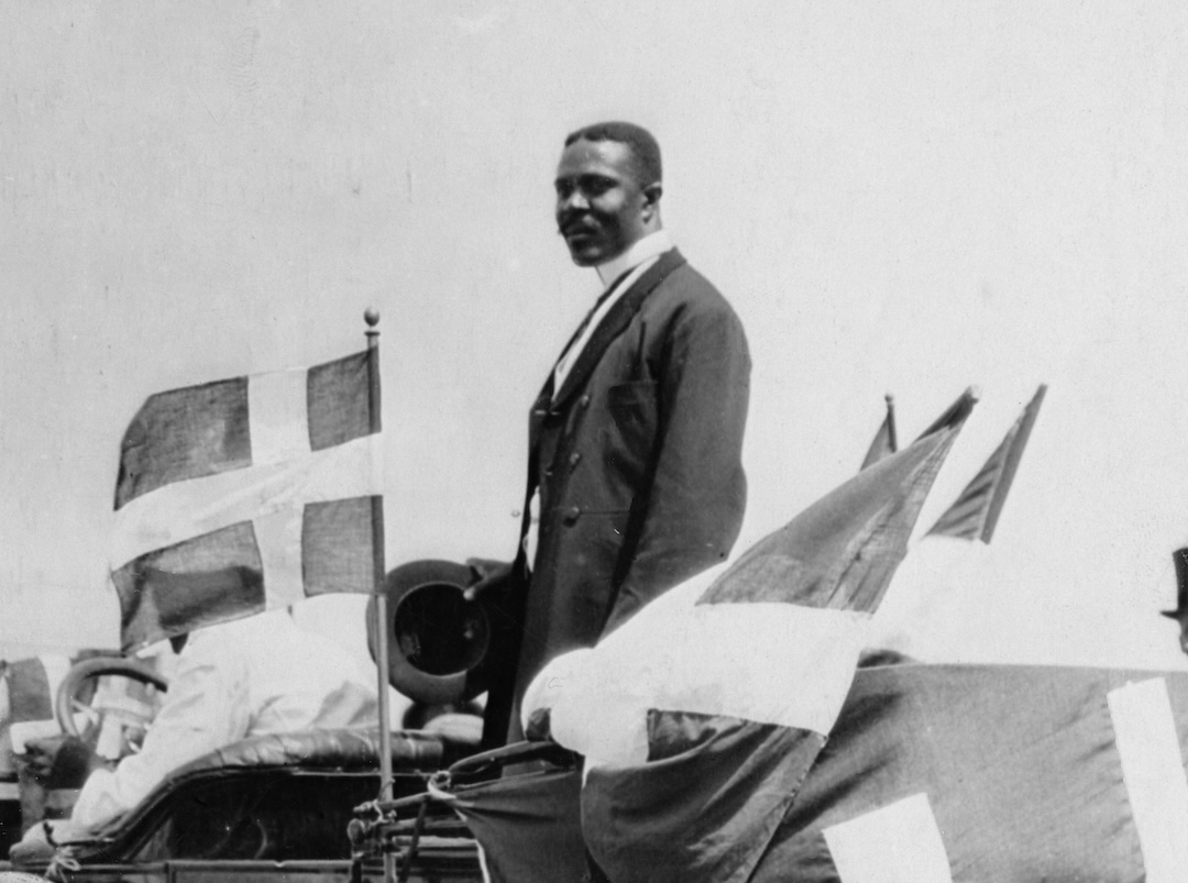 David Hamilton Jackson, founder of the Sankt Croix Labour Union, in Sankt Croix, standing in a car in the Danish West Indies, circa 1915. His car is flying the flag of Denmark.