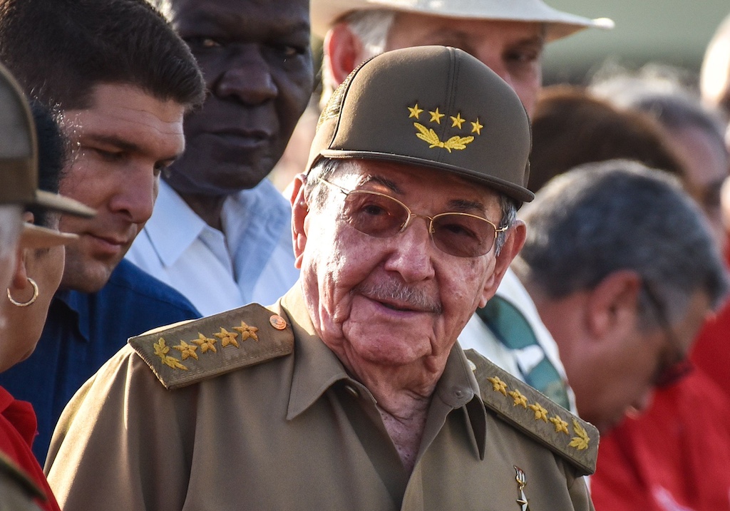 Raúl Castro wearing sunglasses and a green military hat with people surrounding him.