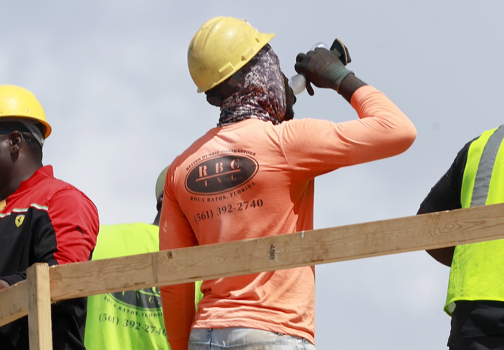 A man with a hard hat on drinking from a water bottle. 