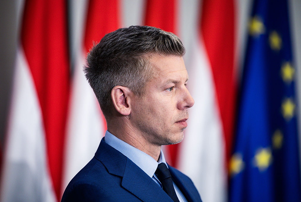 Peter Magyar's profile against a wall of Hungarian flags and one EU flag.