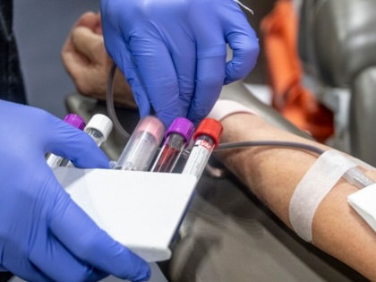 An arm outstretched with two gloved hands holding blood viles next to an IV in the arm.