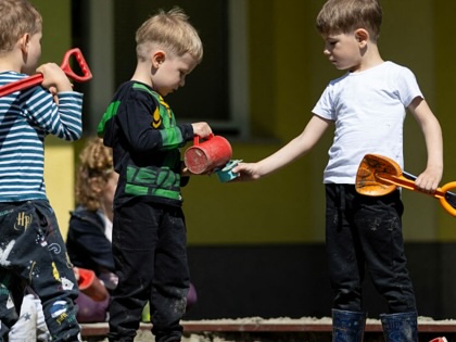 Three preschool-aged boys play with toys in a sandbox.