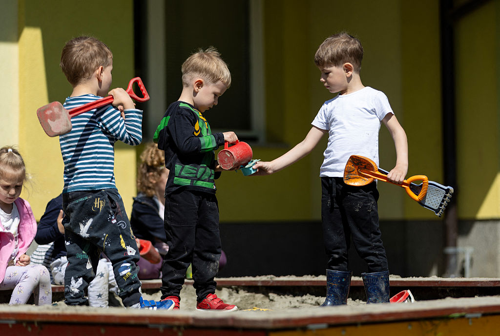 Three preschool-aged boys play with toys in a sandbox.