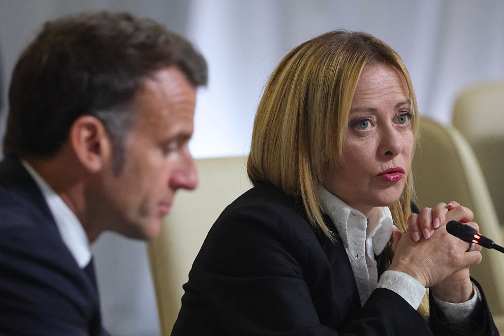 Giorgia Meloni speaking into a microphone with Emmanuel Macron in the foreground.