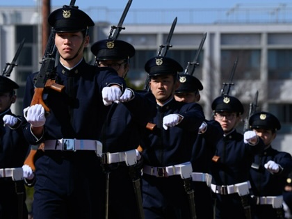 A line of Japanese soldiers stands in formation with rifles pointed upward.