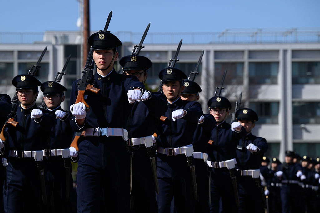 A line of Japanese soldiers stands in formation with rifles pointed upward.