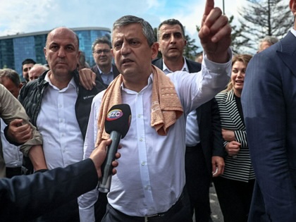 Ozgur Özel speaking into a microphone held by a member of the media while surrounded by party supporters.