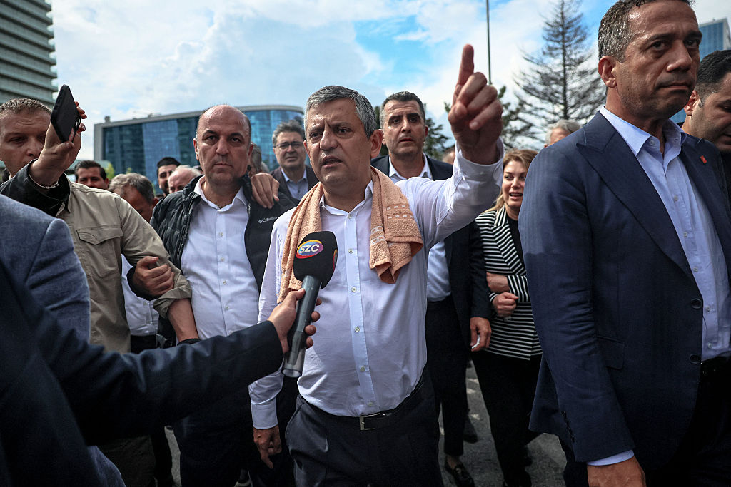 Ozgur Özel speaking into a microphone held by a member of the media while surrounded by party supporters.