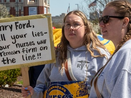 Two nurses on strike, one holds a sign that says, "Henry Ford, tell your lies—your nurses will remain firm on the line!"