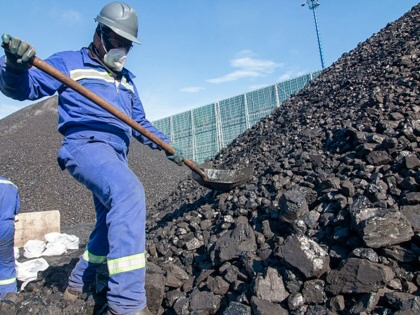 A man with a shovel standing on a large mound of coal.