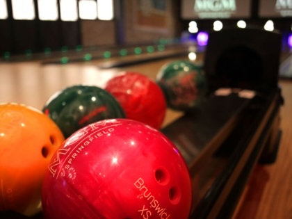 Five bowling balls sit in the ball return rack with two bowling lanes in the background.