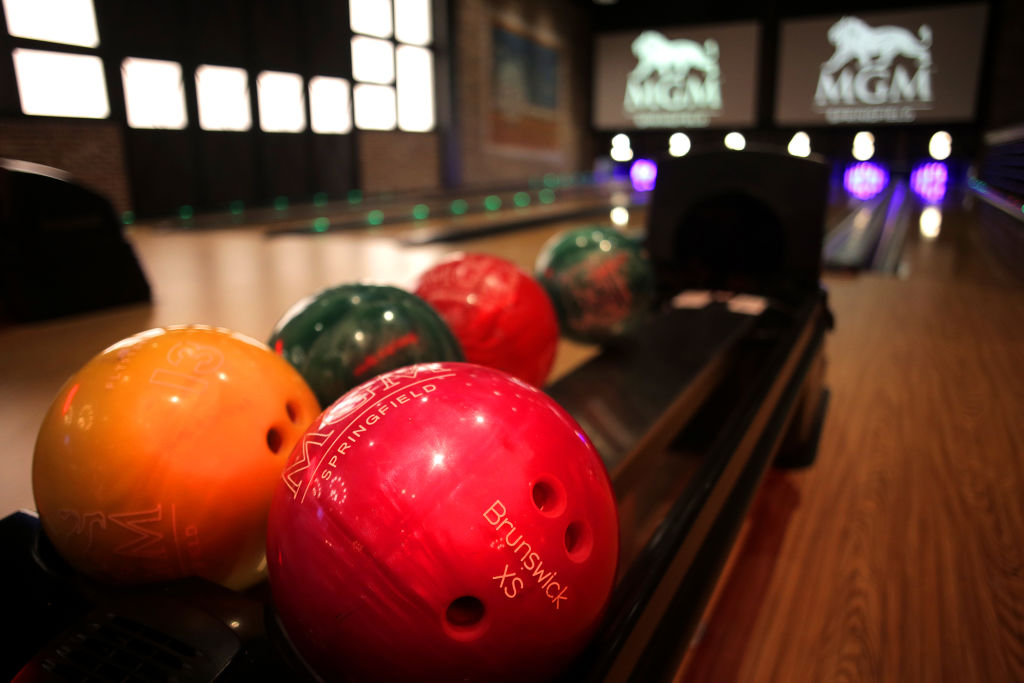 Five bowling balls sit in the ball return rack with two bowling lanes in the background.