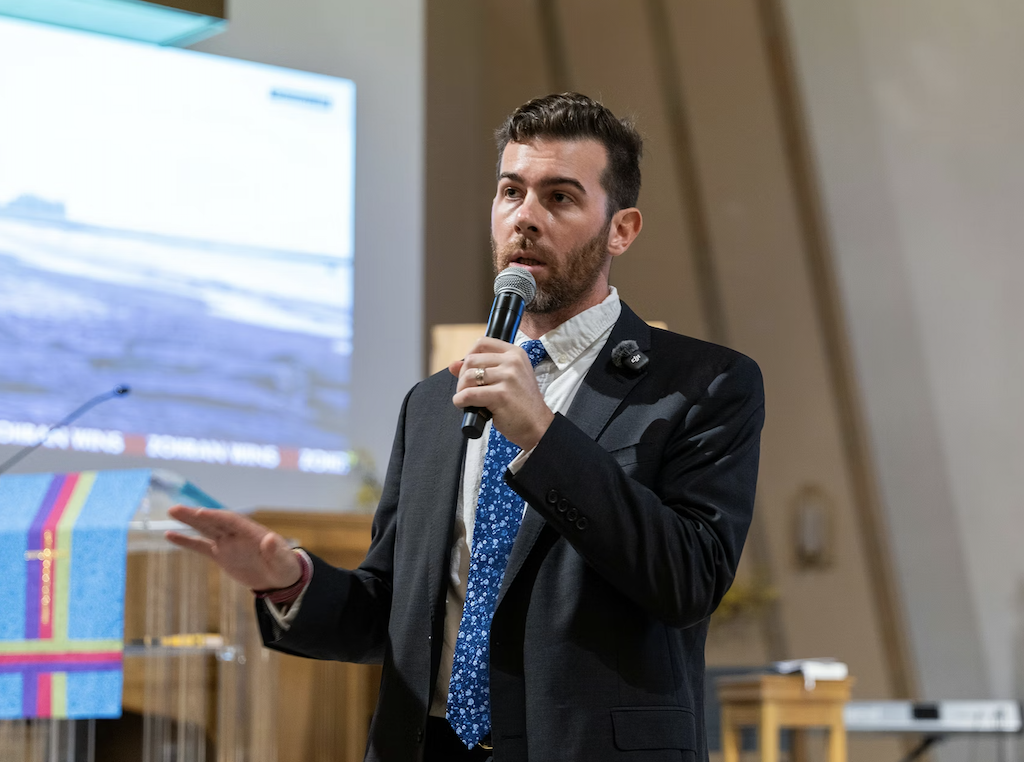 Oliver Larking speaking into a microphone while gesturing. 