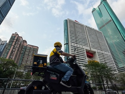 A delivery rider drives an electric scooter past skyscrapers in Shenzhen, China.
