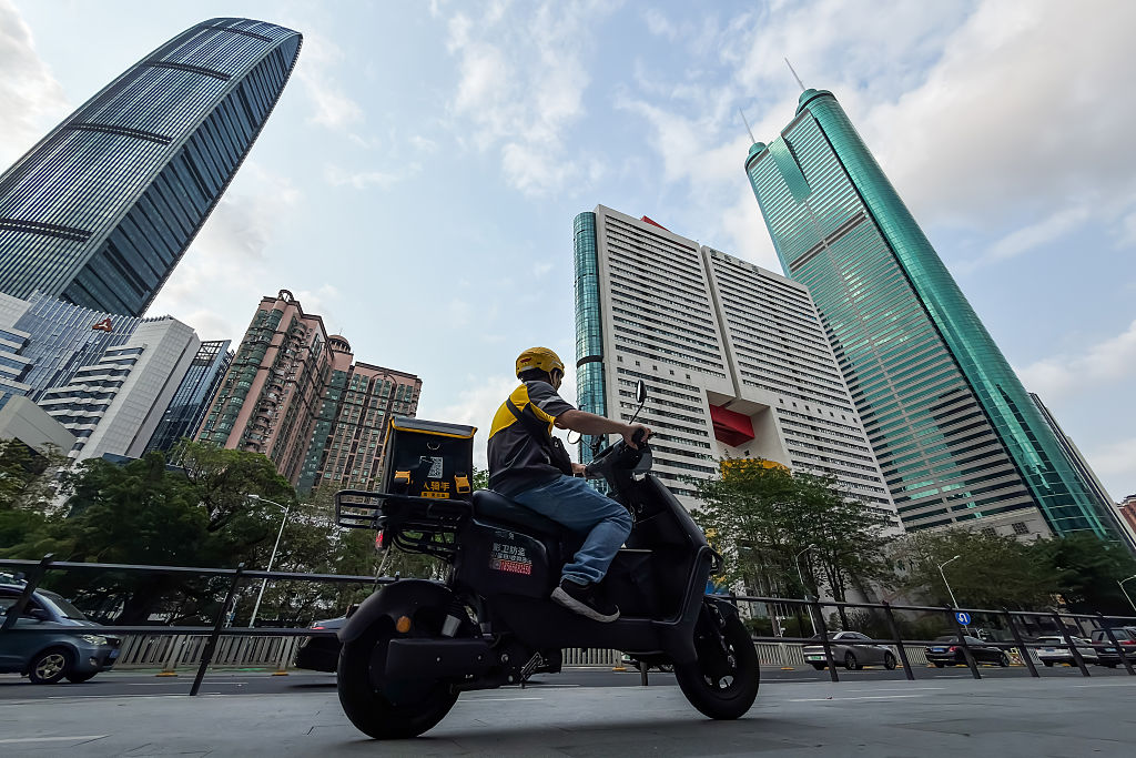 A delivery rider drives an electric scooter past skyscrapers in Shenzhen, China.