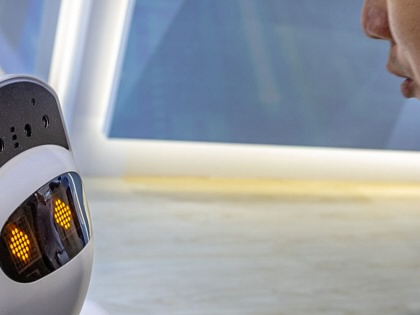 An attendee looks closely at a small social companion robot with illuminated digital eyes at a technology booth during COMPUTEX in Taipei on June 3, 2026.