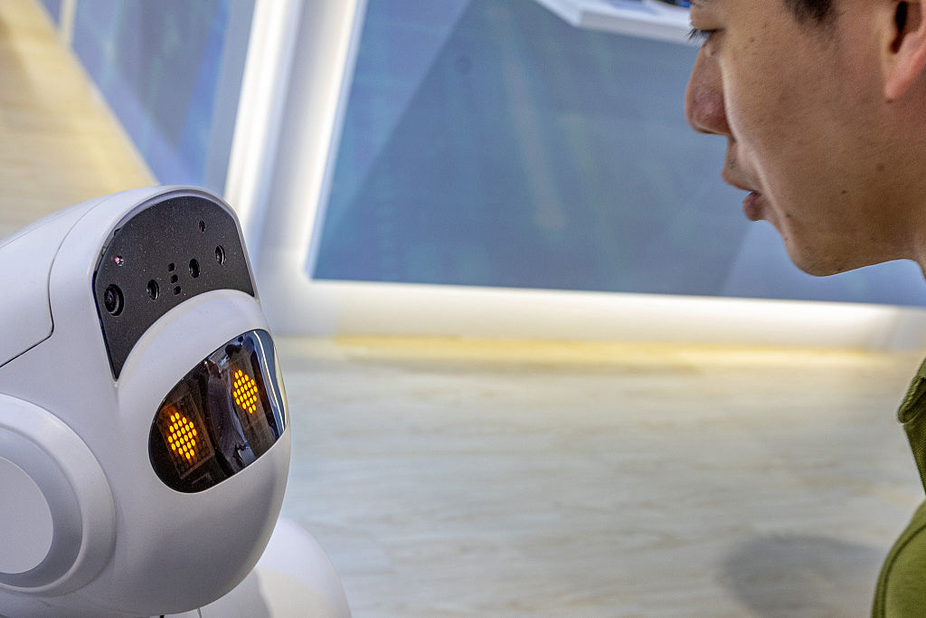 An attendee looks closely at a small social companion robot with illuminated digital eyes at a technology booth during COMPUTEX in Taipei on June 3, 2026.