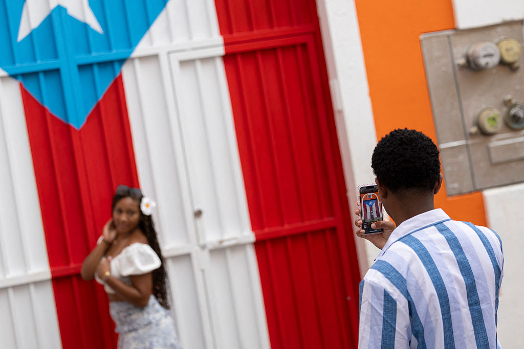 A man photographs a woman in front of a Puerto Rican flag mural in Old San Juan.