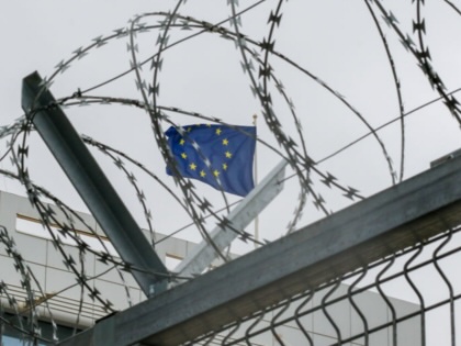 A flag representing the European Union is photographed through barbed wire. 