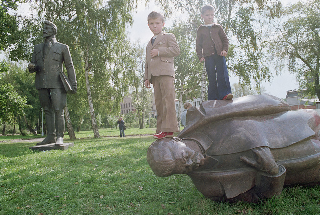 Children stand on a fallen statue of Joseph Stalin.