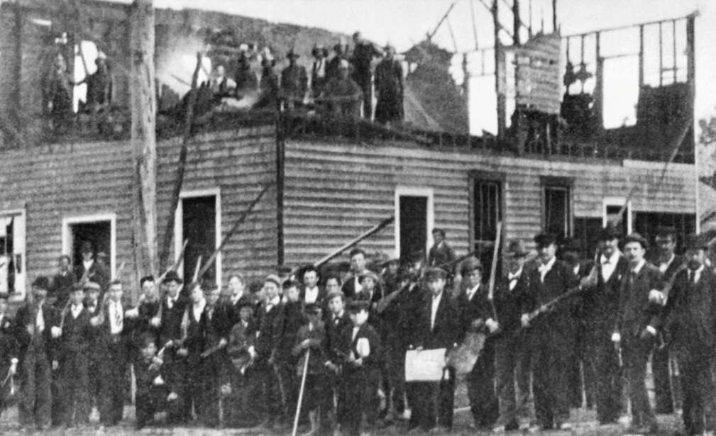 Armed militiamen stand in front and atop the burned building of the black newspaper, the Daily Record.