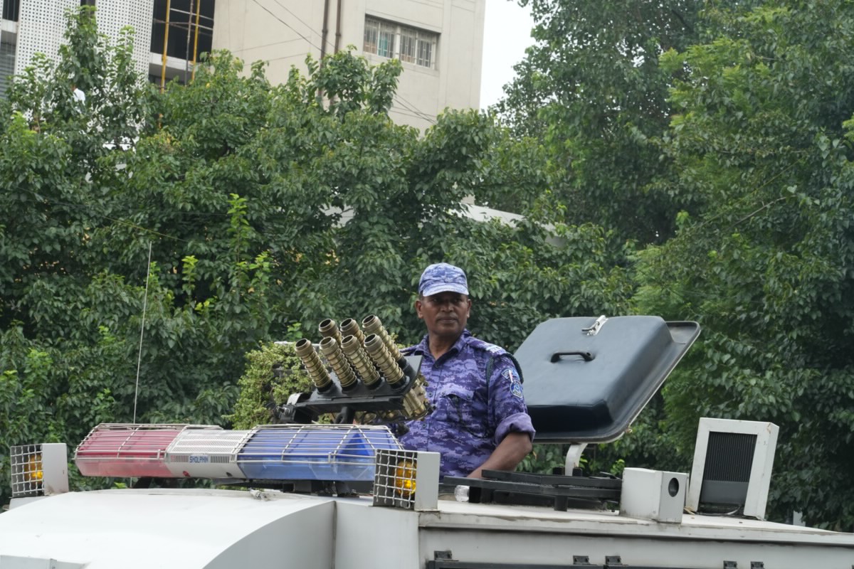 A security officer stands on top of an armored police vehicle fitted with a multibarrel tear gas launcher.