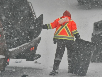 A garbage man empties cans of garbage into a garbage truck as a snowstorm hits Toronto on December 26, 2025.