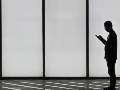 A man uses a smartphone while standing in front of an illuminated wall on April 27, 2026, in Shenzhen, Guangdong Province, China