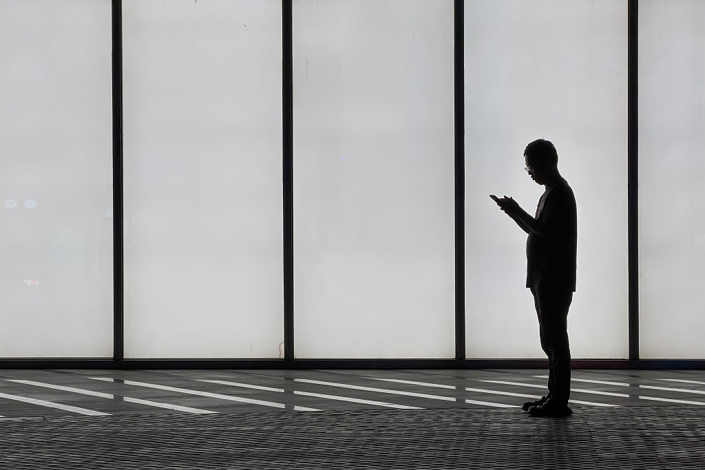 A man uses a smartphone while standing in front of an illuminated wall on April 27, 2026, in Shenzhen, Guangdong Province, China