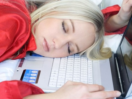 A woman falls asleep at her laptop.