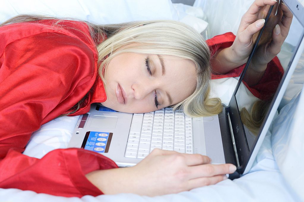 A woman falls asleep at her laptop.