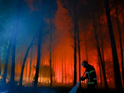 A firefighter hoses down the charred ground as flames continue to burn in the Landes forest in Luglon, France, on August 14, 2026.