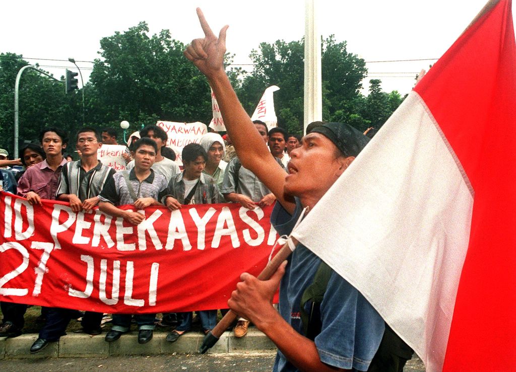 An Indonesian student holding the Indonesian national flag shouts antigovernment slogans while others hold a banner that says "Syarwan is the man behind the 27 July riot," during a protest at the Department of Home Affairs in Jakarta.