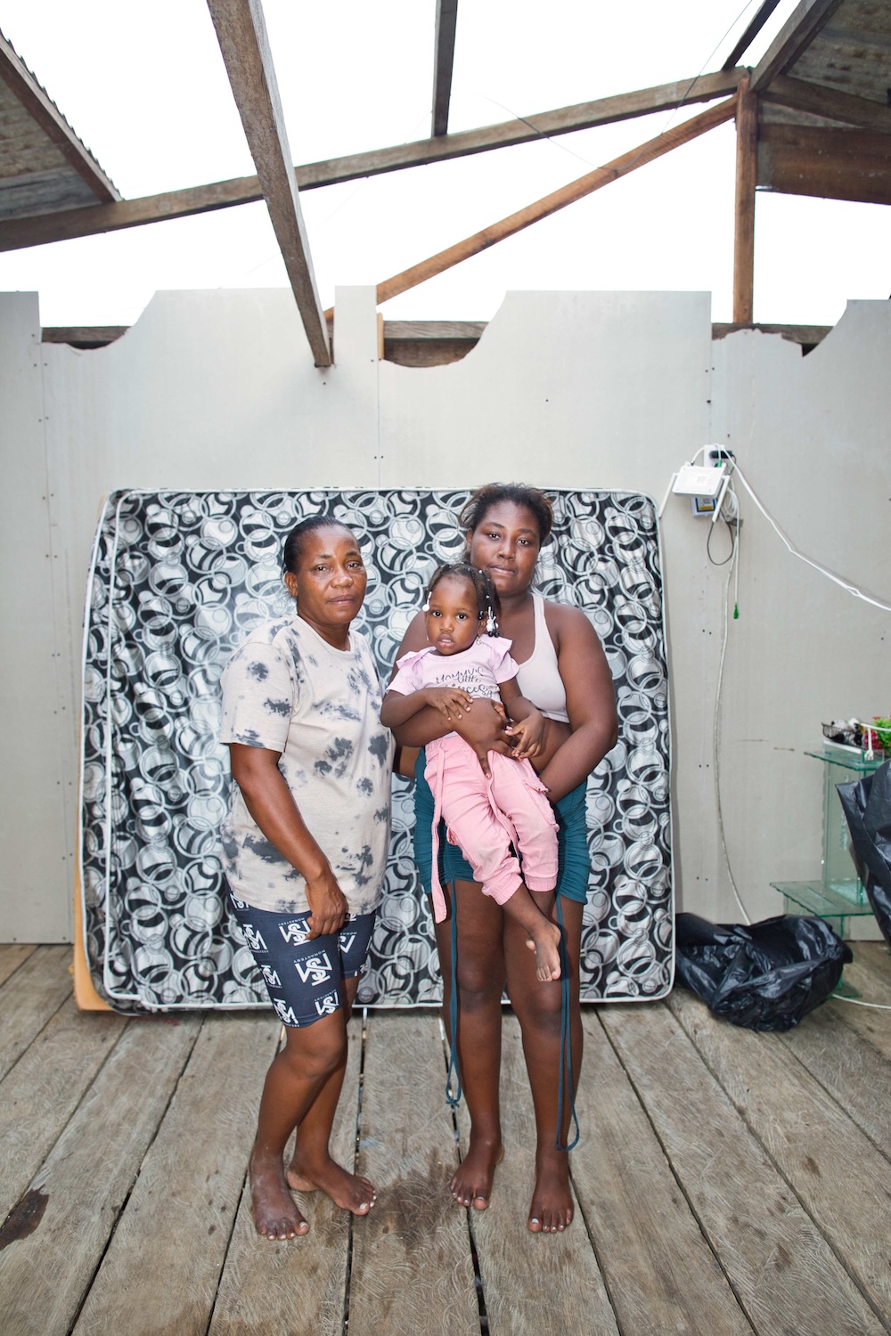Two women and a child are photographed standing in their destroyed home.
